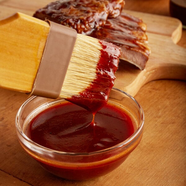 A wooden spoon pouring Cortazzo BBQ sauce into a bowl of ribs.