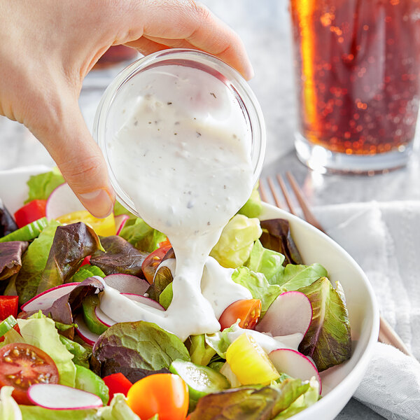 A person pouring Kraft Blue Cheese dressing into a bowl of salad.