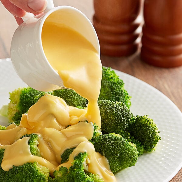 A person pouring LeGout cheese sauce onto a plate of broccoli.