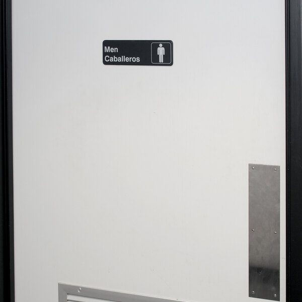 A white door with a black and white Tablecraft Men's Restroom sign.