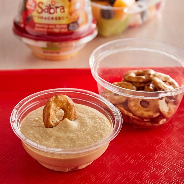 A red bowl of Sabra roasted red pepper hummus with Rold Gold pretzels on a red tray.