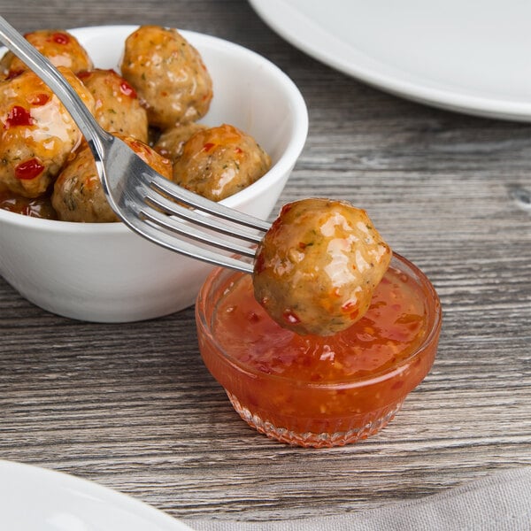 A fork dipping a meatball into a bowl of Frank's RedHot Sweet Chili Sauce.