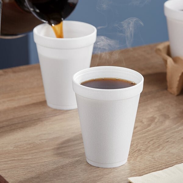 A cup of coffee being poured into a Dart white foam cup on a white table.