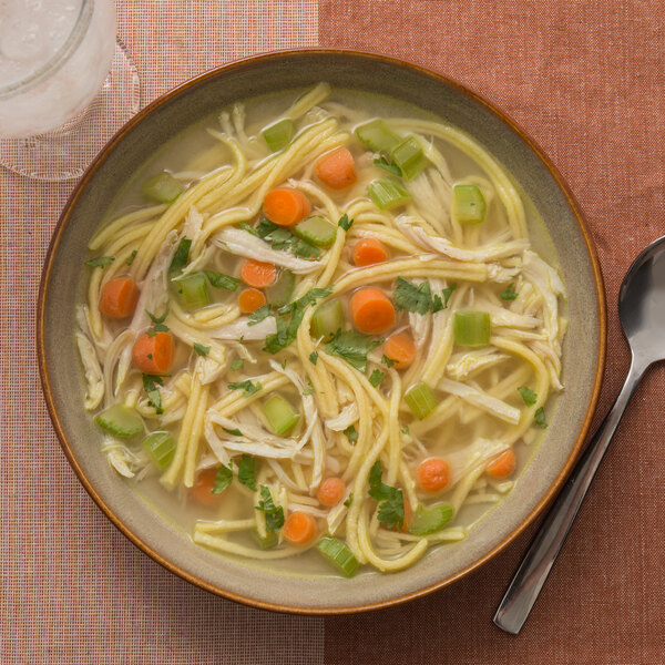 A bowl of chicken noodle soup with Little Barn Homemade Fine Egg Noodles, carrots, and celery.