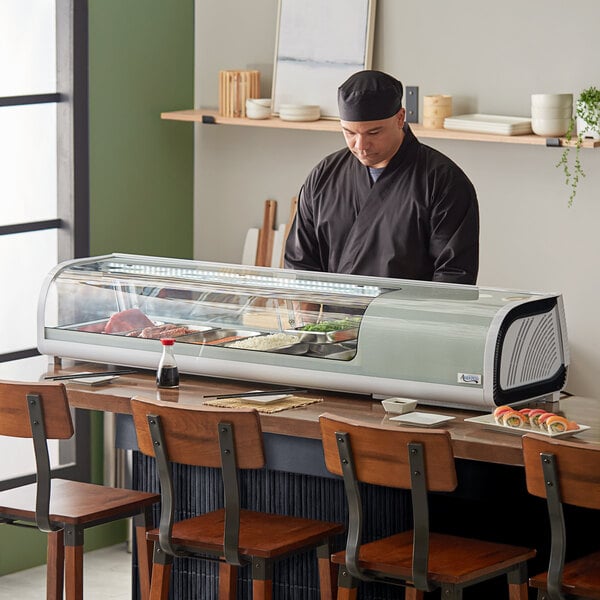 An Avantco countertop refrigerated sushi display case on a counter filled with food trays.