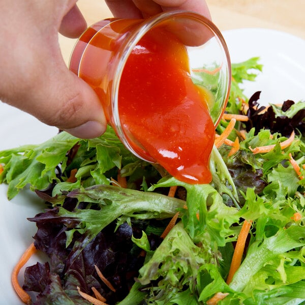 A hand pouring Ken's California French Dressing over a salad.