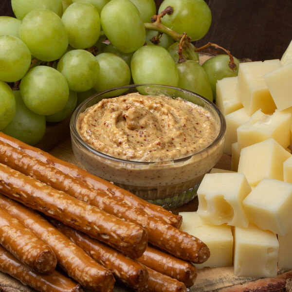 A plate of food with pretzels, cheese, and grapes with a bowl of Pilsudski Polish Style Horseradish Mustard.