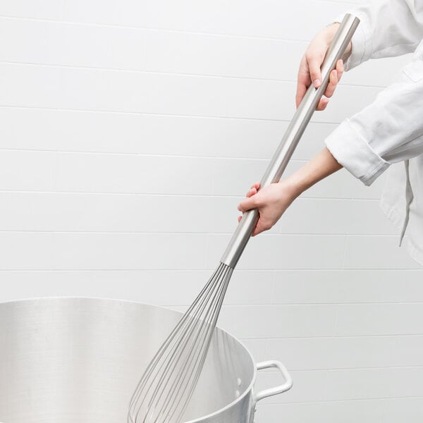 A hand holding a Carlisle stainless steel French whisk in a pot.