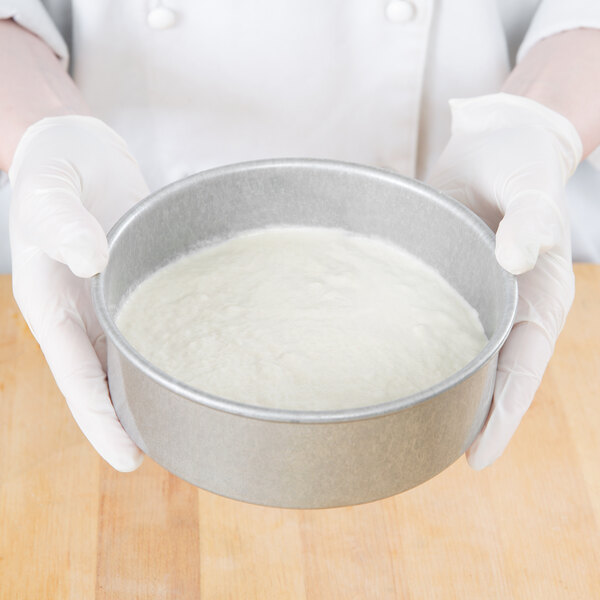 A person in white gloves using a Chicago Metallic round cake pan.