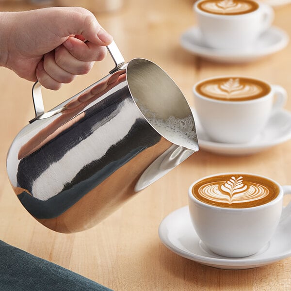 A person pouring milk into a cup of coffee using a Choice polished stainless steel frothing pitcher.