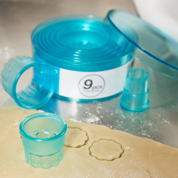 A blue plastic container of Ateco fluted round cookie cutters on a counter.