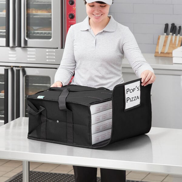 A woman holding a black Choice insulated pizza delivery bag with white pizza boxes inside.