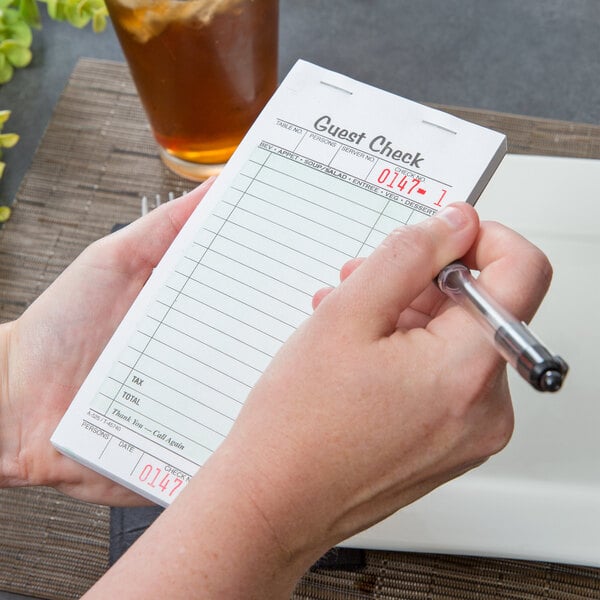 A person using an Adams guest check book to write a receipt at a restaurant counter.