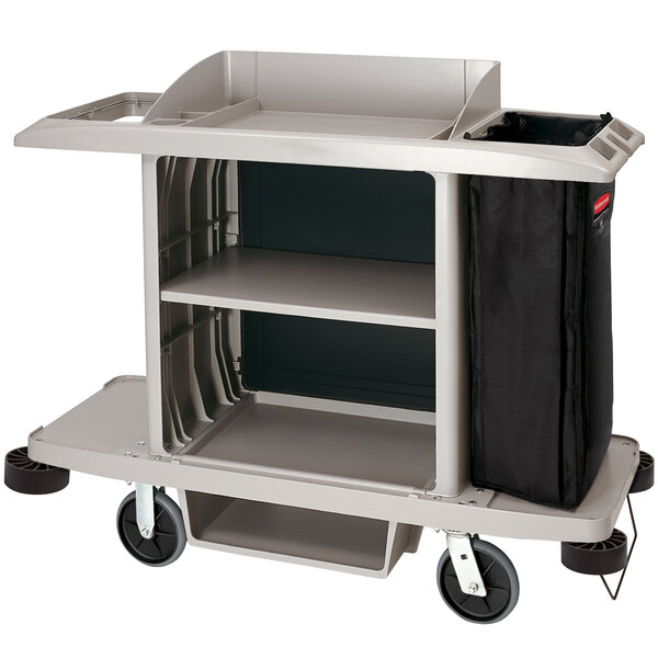 A Rubbermaid housekeeping cart with a black bag on the bottom shelf.