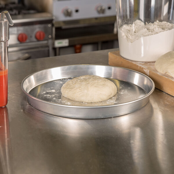 A dough on an American Metalcraft heavy weight aluminum pizza pan on a counter.