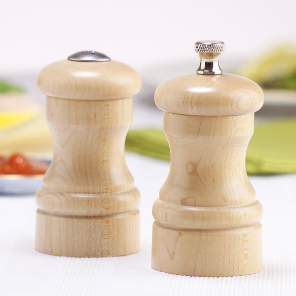 A close-up of a wooden pepper grinder with salt and pepper shakers on a table.