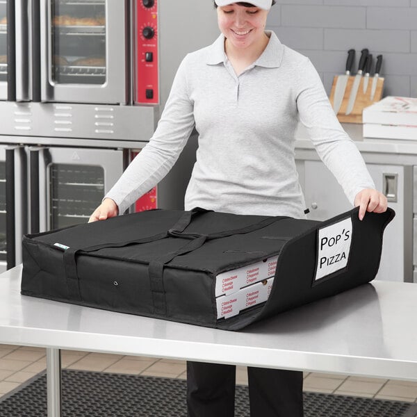 A woman holding a black Choice insulated pizza bag with white pizza boxes inside.
