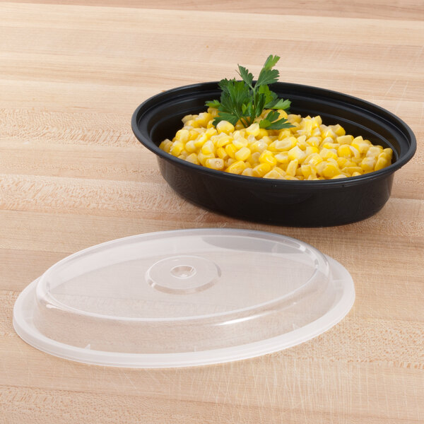 A black Pactiv Newspring VERSAtainer oval microwavable container filled with corn and topped with a lid.
