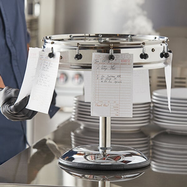 A person using a Choice stainless steel pedestal order wheel ticket holder.