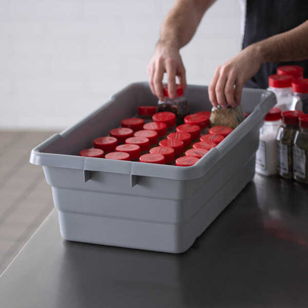 A person putting jars of seasoning in a gray Channel Polyethylene lug with red caps.