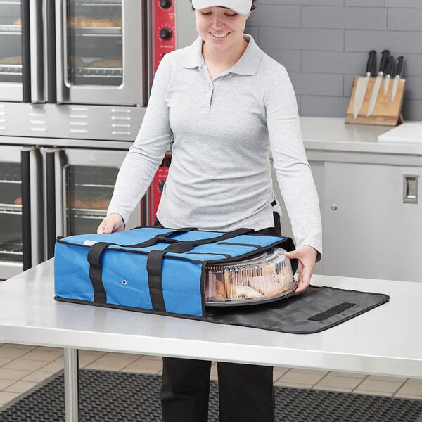 A woman in a chef hat holding a blue Choice insulated deli tray bag with a black strap.