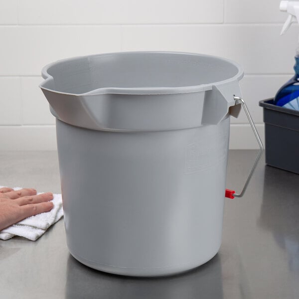 A person placing a Rubbermaid gray bucket on a counter.