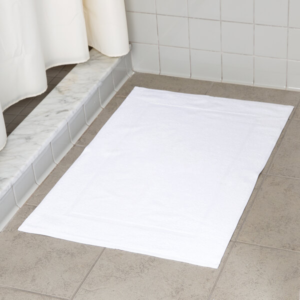 An Oxford Belleeza white 100% ringspun cotton bath mat on a tile floor.