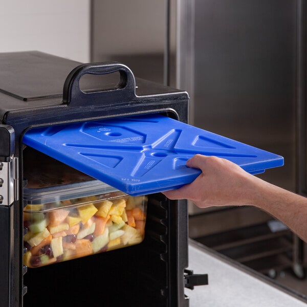 A hand using a blue CaterGator ice board to hold food in a blue plastic container.