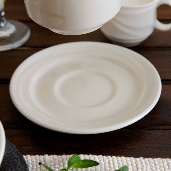 A close up of a Oneida cream white saucer on a table.