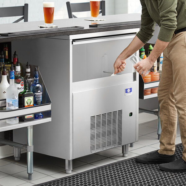 A Manitowoc undercounter ice machine on a counter in a bar with a person putting ice in a glass.