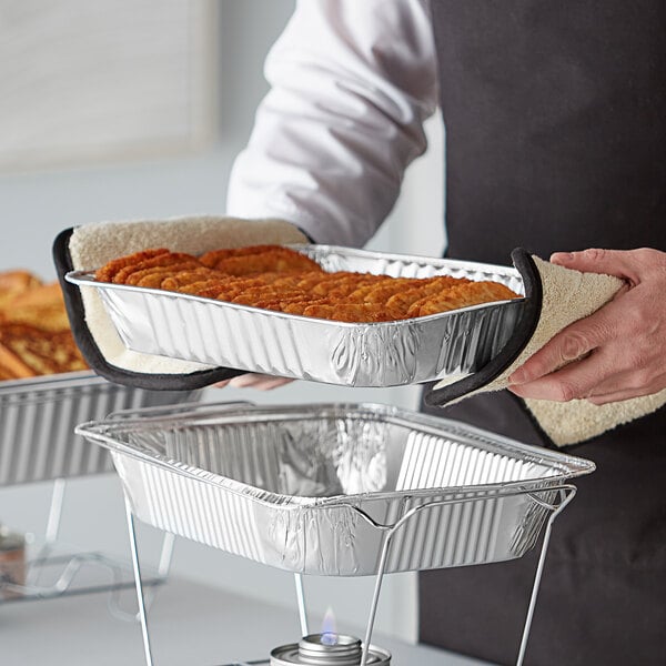A person holding a tray of food in a Choice medium foil steam table pan.