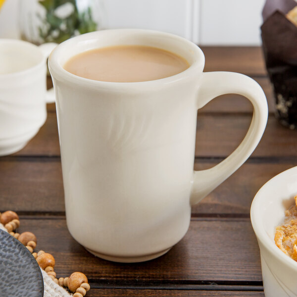 A white Oneida mug filled with brown liquid next to a bowl of cereal.