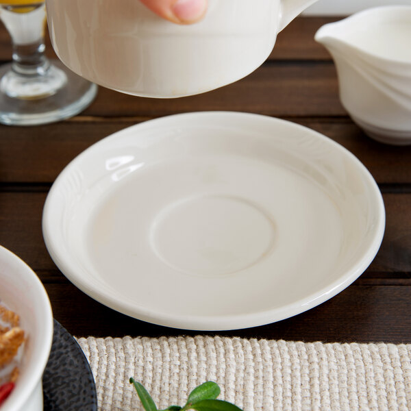 A hand pouring a white pitcher into a Oneida cream white Odyssey saucer.