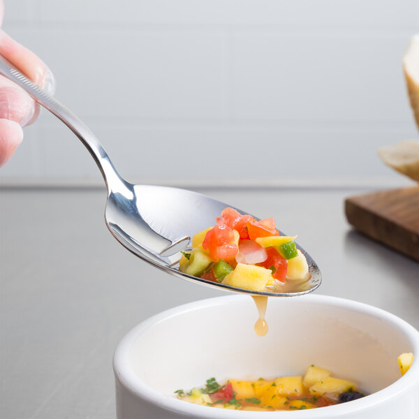 A hand using a Mercer Culinary stainless steel slotted bowl plating spoon to serve fruit and vegetable soup.
