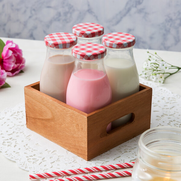 Acopa glass milk bottles in a wooden crate on a table with a red and white checkered tablecloth.