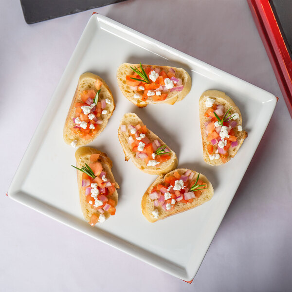 A Frilich white china display plate with small appetizers on a table.