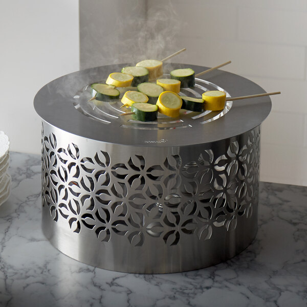 A Rosseto stainless steel warmer stand with a grill holding zucchini and squash on skewers.