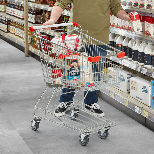 A man pushing a Regency Supermarket shopping cart full of products in a grocery store aisle.