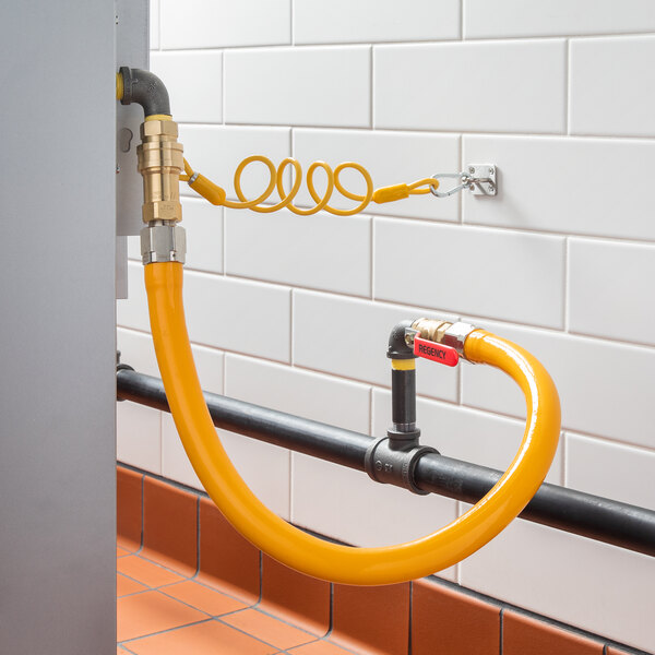A yellow Regency gas connector hose kit connected to a metal pipe.