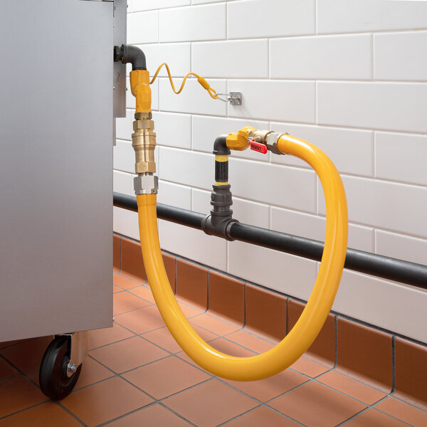 A yellow Regency gas connector hose kit connected to a metal pipe with black fittings.