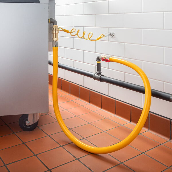 A yellow Regency gas connector hose with elbows and a quick disconnect connected to a pipe.
