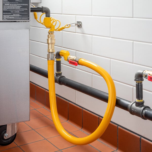 A yellow Regency gas connector hose with swivel connectors and a quick disconnect connected to a metal pipe.