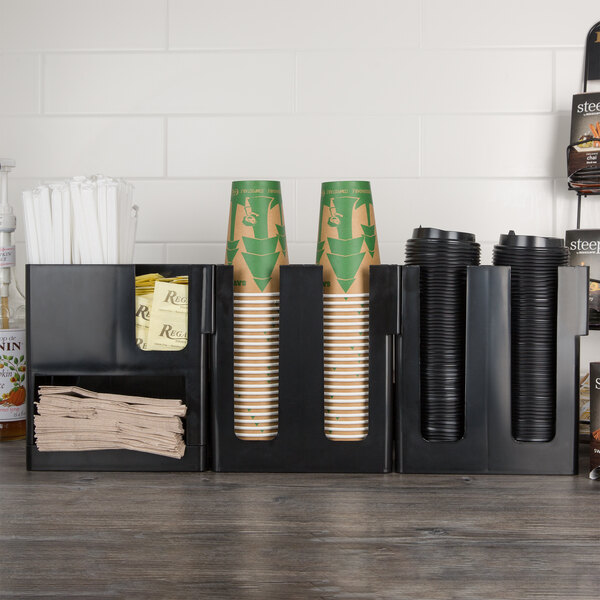 A black Choice countertop cup, lid, and napkin organizer holding coffee cups.