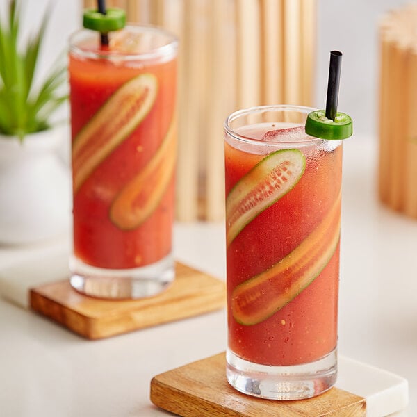 Two glasses of Campbell's tomato juice with cucumber slices and straws on a table with a white and black striped placemat.