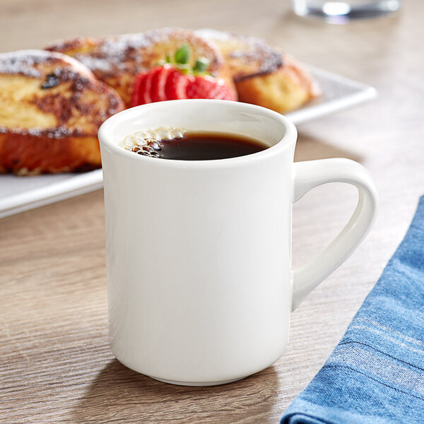 An Acopa ivory stoneware mug filled with coffee on a table with a strawberry.