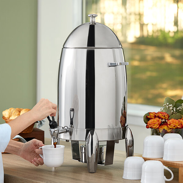 A woman using a Choice stainless steel coffee urn to pour coffee into a white mug.