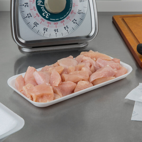 A white CKF foam meat tray of raw chicken on a counter.