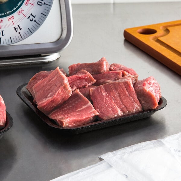 A black CKF foam meat tray holding raw meat on a counter.