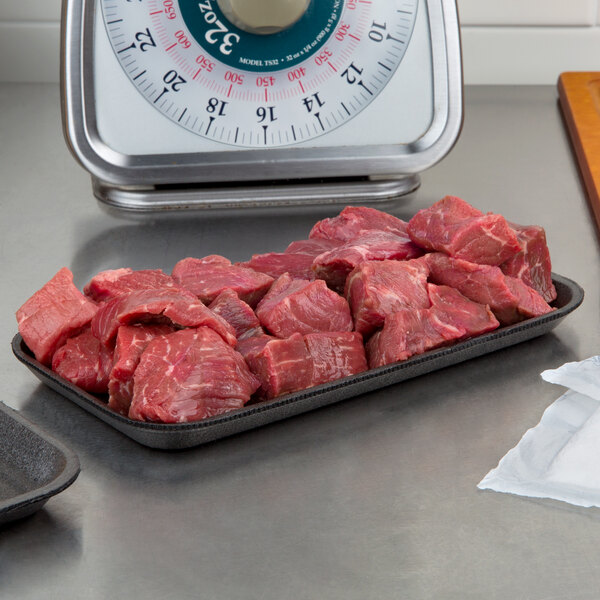 A black foam CKF meat tray on a counter with raw meat.