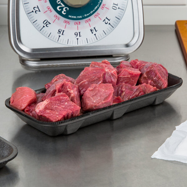 A black CKF foam meat tray on a counter full of raw meat.